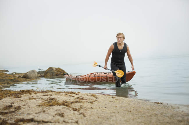 650x433 man in a wetsuit drawing his kayak tranquil scene, copy space - Wetsuit Drawing