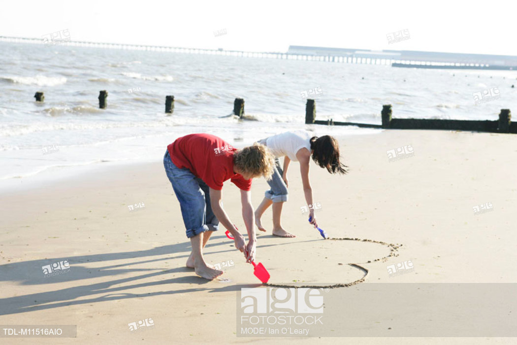 1050x700 a young couple drawing a heart shape in the sand, stock photo - Young Couple Drawing