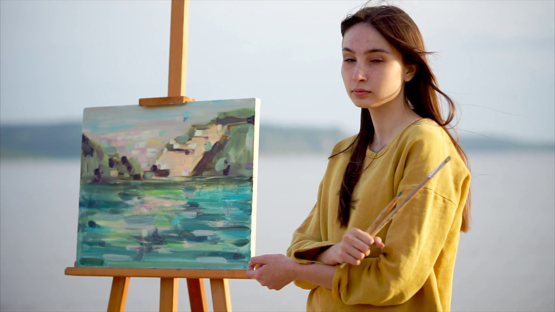 1920x1080 A Romantic Adult Girl Stands Near Her Still Life Next To The Sea - Woman Painting On Canvas